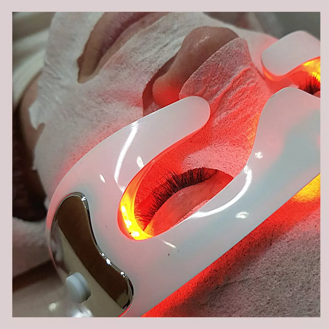 Una clienta en cabina con máscara de tela y la máscara de luz LED Therapy encendida